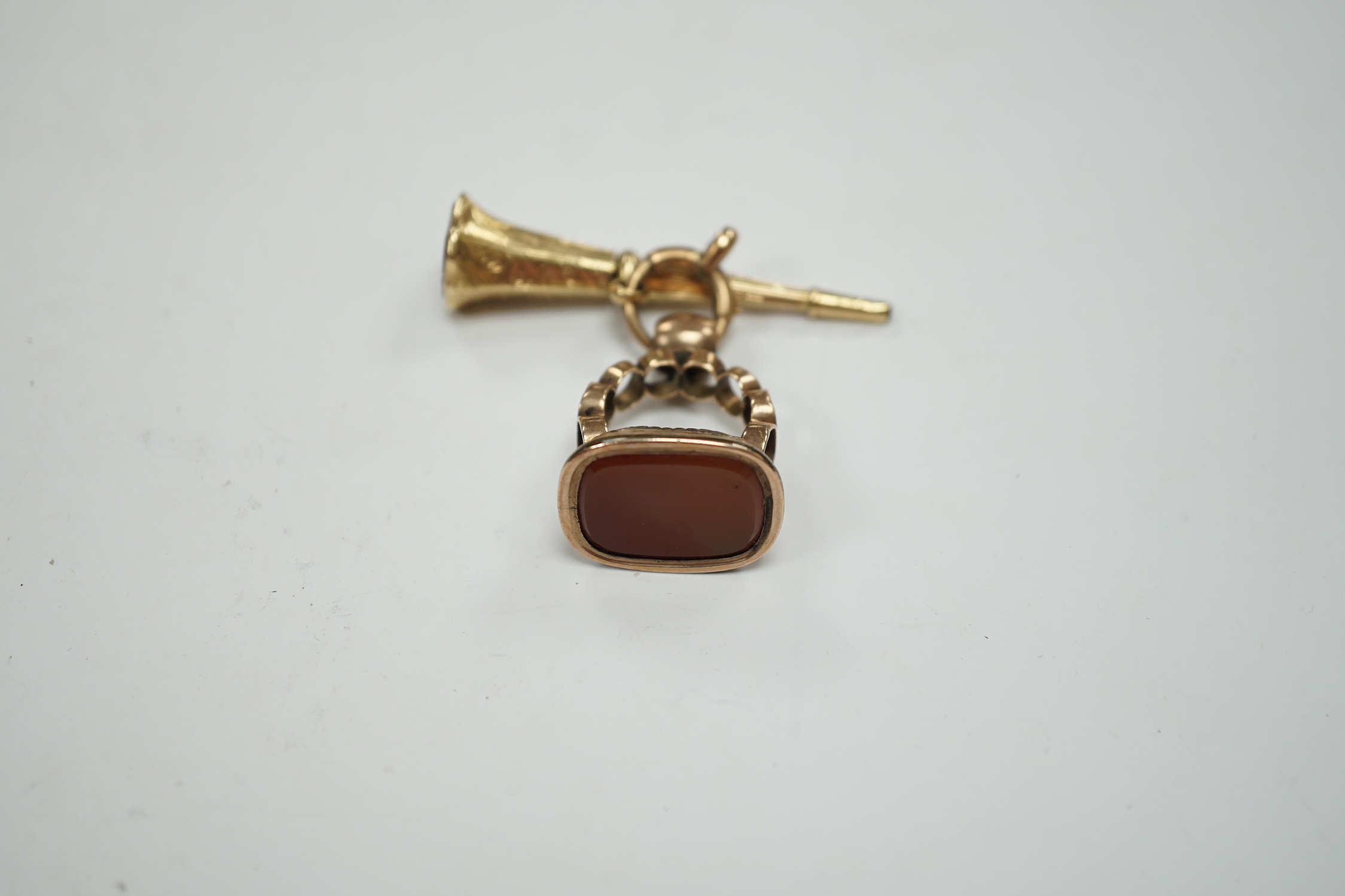 A 19th century engraved yellow metal overlaid and carnelian set trumpet shaped watch key, the matrix carved with crest and initial, 51mm, together with a 19th century gold plated and carnelian set fob.